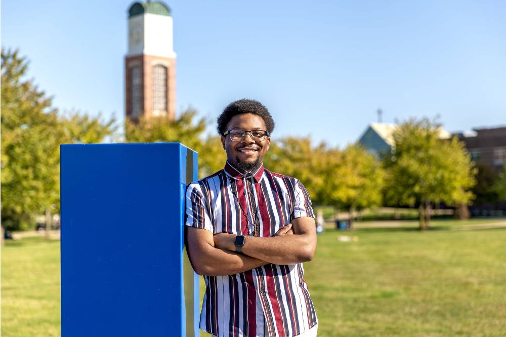 Image 1 of 2 Man standing in grassy area with arms crossed, smiling